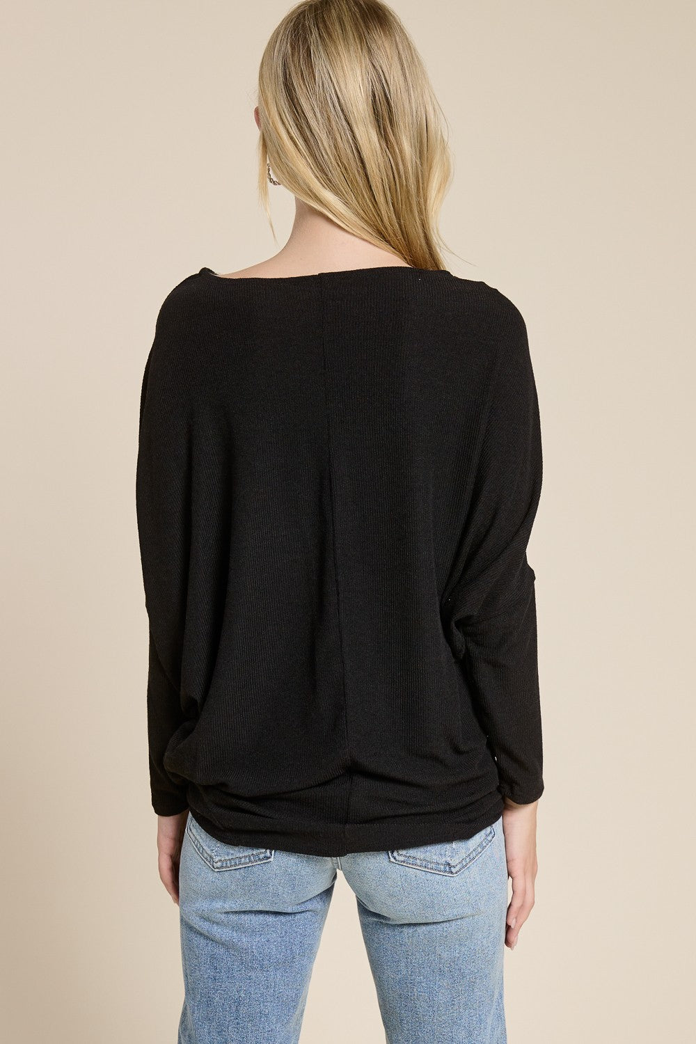 woman wearing a loose black long sleeve shirt with a wide neckline and relaxed fit, paired with light wash jeans