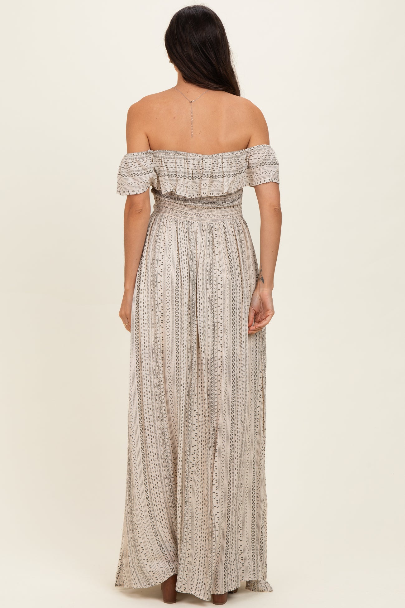 woman wearing a back view of a beige off-the-shoulder maxi dress with a smocked bodice and vertical stripes