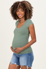 woman wearing a green short sleeve maternity top and holding her baby bump, paired with denim shorts