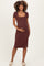 woman wearing a rust brown maternity dress with short sleeves and a side slit, holding her baby bump