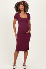 woman wearing a burgundy short sleeve maternity dress with a square neckline and holding her baby bump