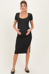 woman wearing a black ribbed short sleeve maternity dress with a side slit and holding her baby bump