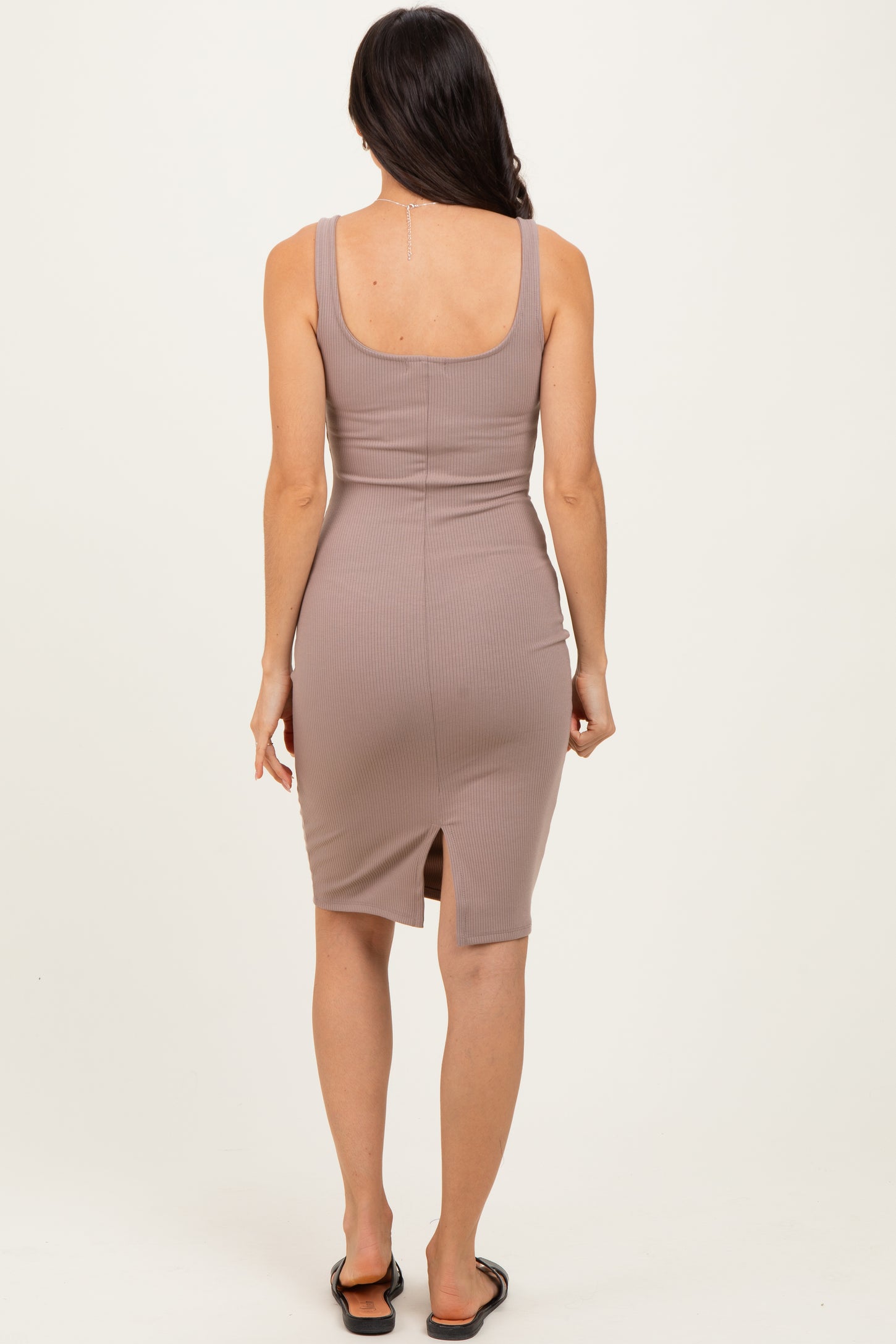 woman wearing a taupe ribbed midi dress with a scooped back and a back slit, seen from the back