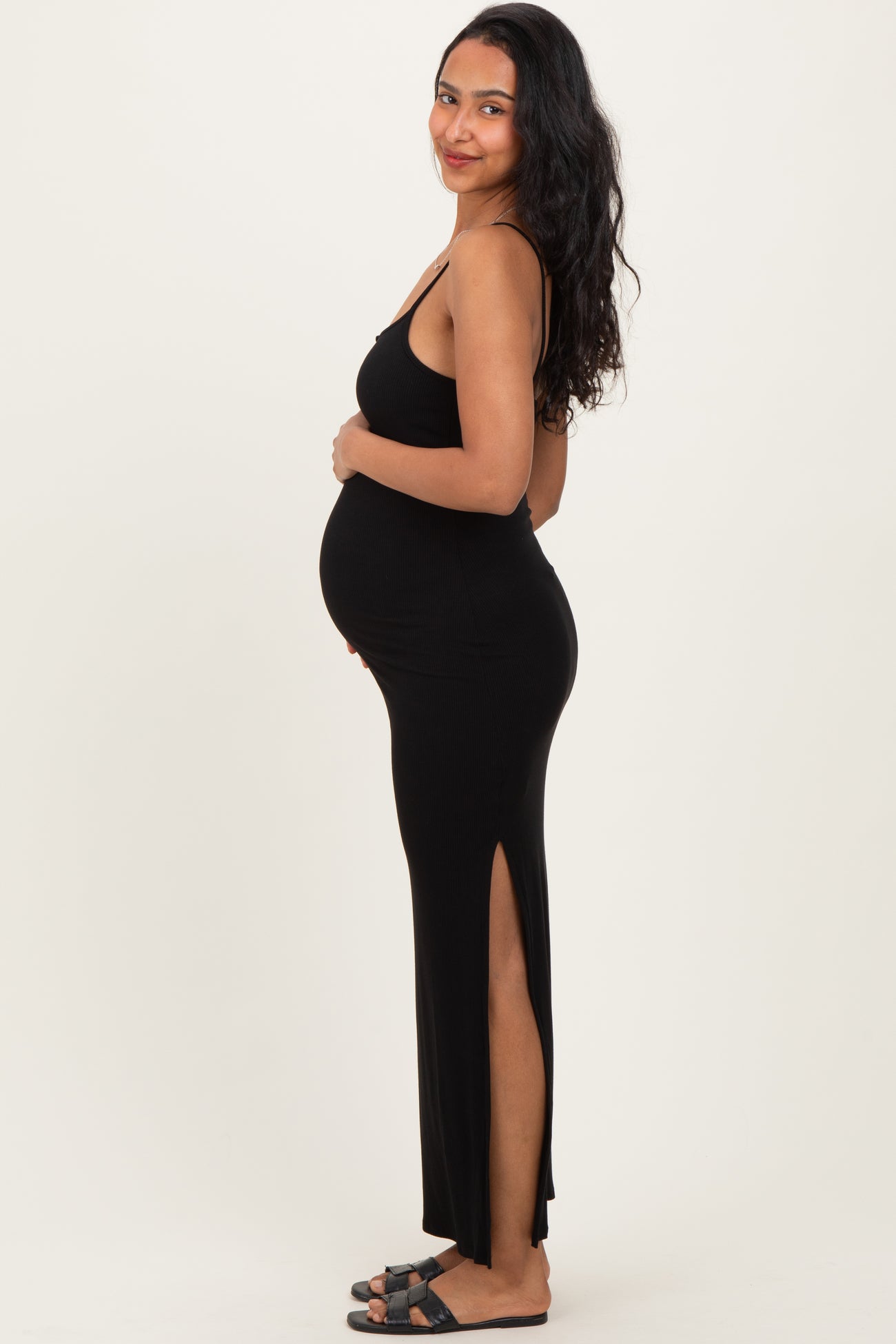 woman wearing a black ribbed maternity dress with side slits and holding her baby bump