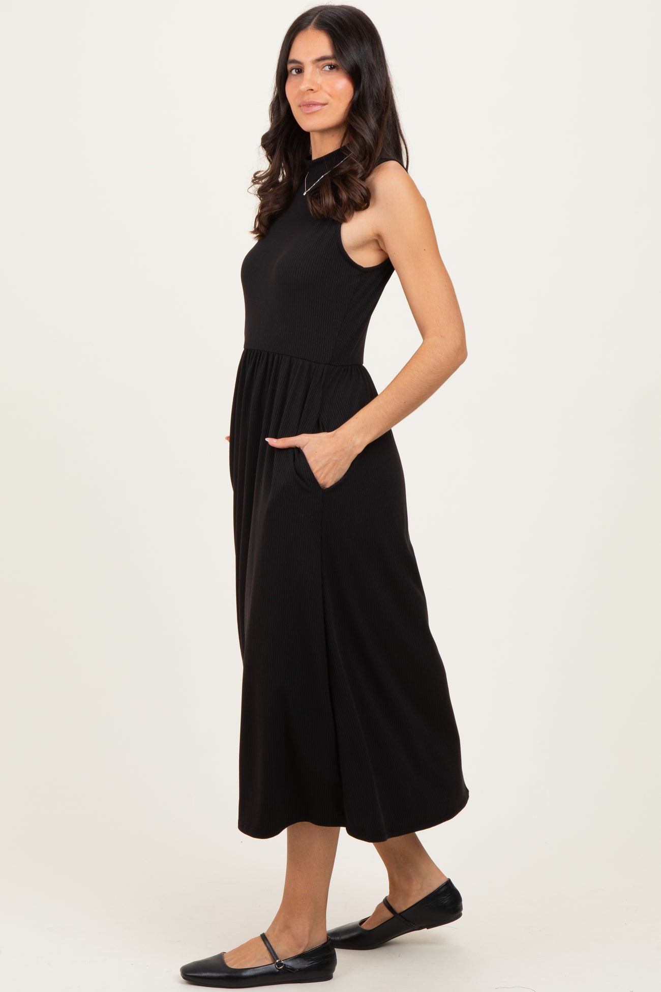 woman wearing a black sleeveless midi dress with a fitted bodice and side pockets
