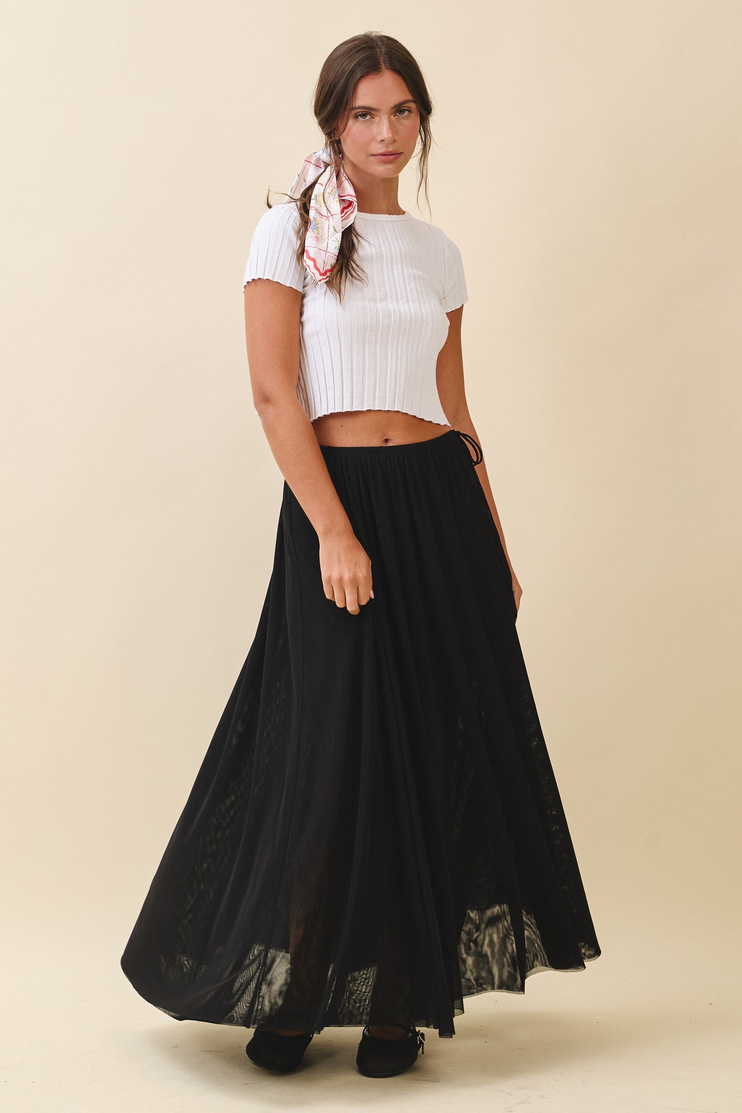 woman wearing a white ribbed crop top and a black flowy maxi skirt, styled with a printed scarf in her hair