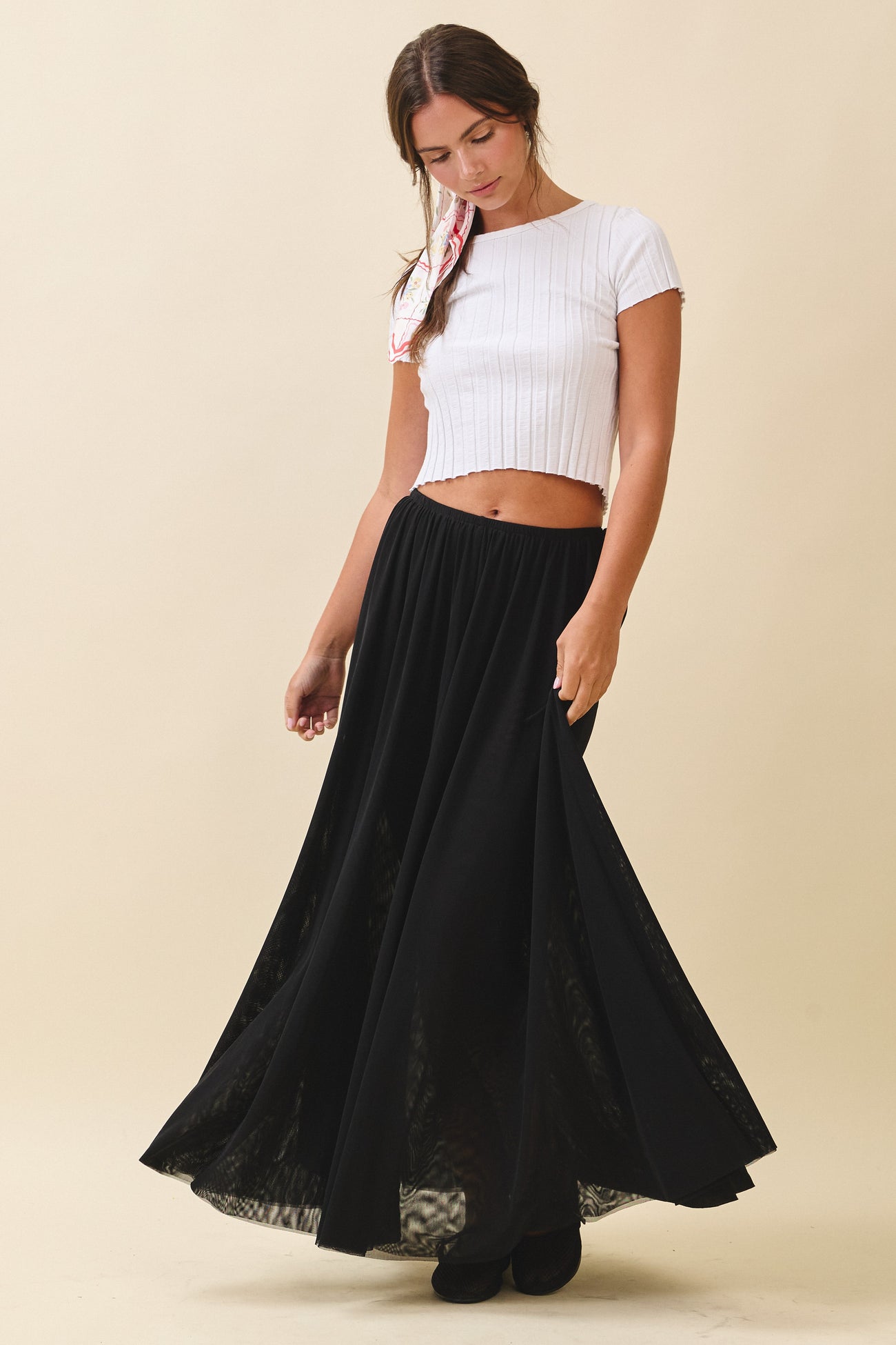 woman wearing a white cropped ribbed top and a long black flowy skirt, posing with a soft smile