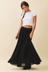 woman wearing a white cropped ribbed top and a long black flowy skirt, posing with a soft smile