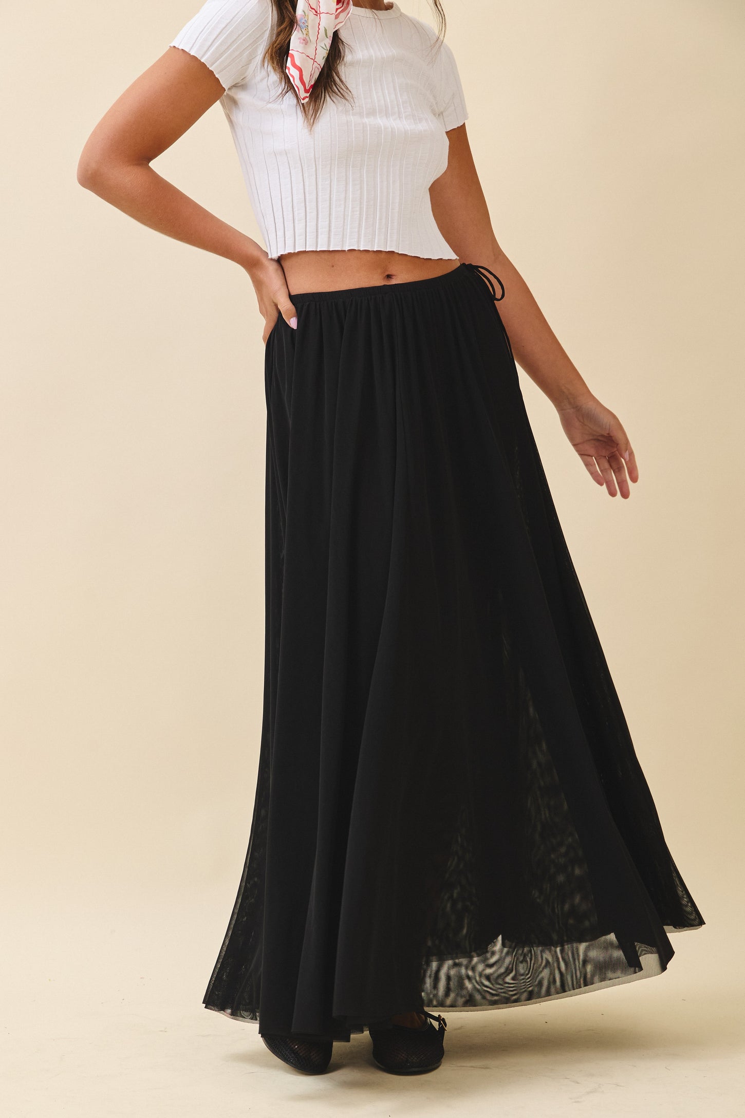woman wearing a black flowing maxi skirt and a white cropped top with a colorful scarf in her hair