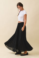 woman wearing a fitted white cropped top and a flowy black maxi skirt, standing and looking down at the skirt