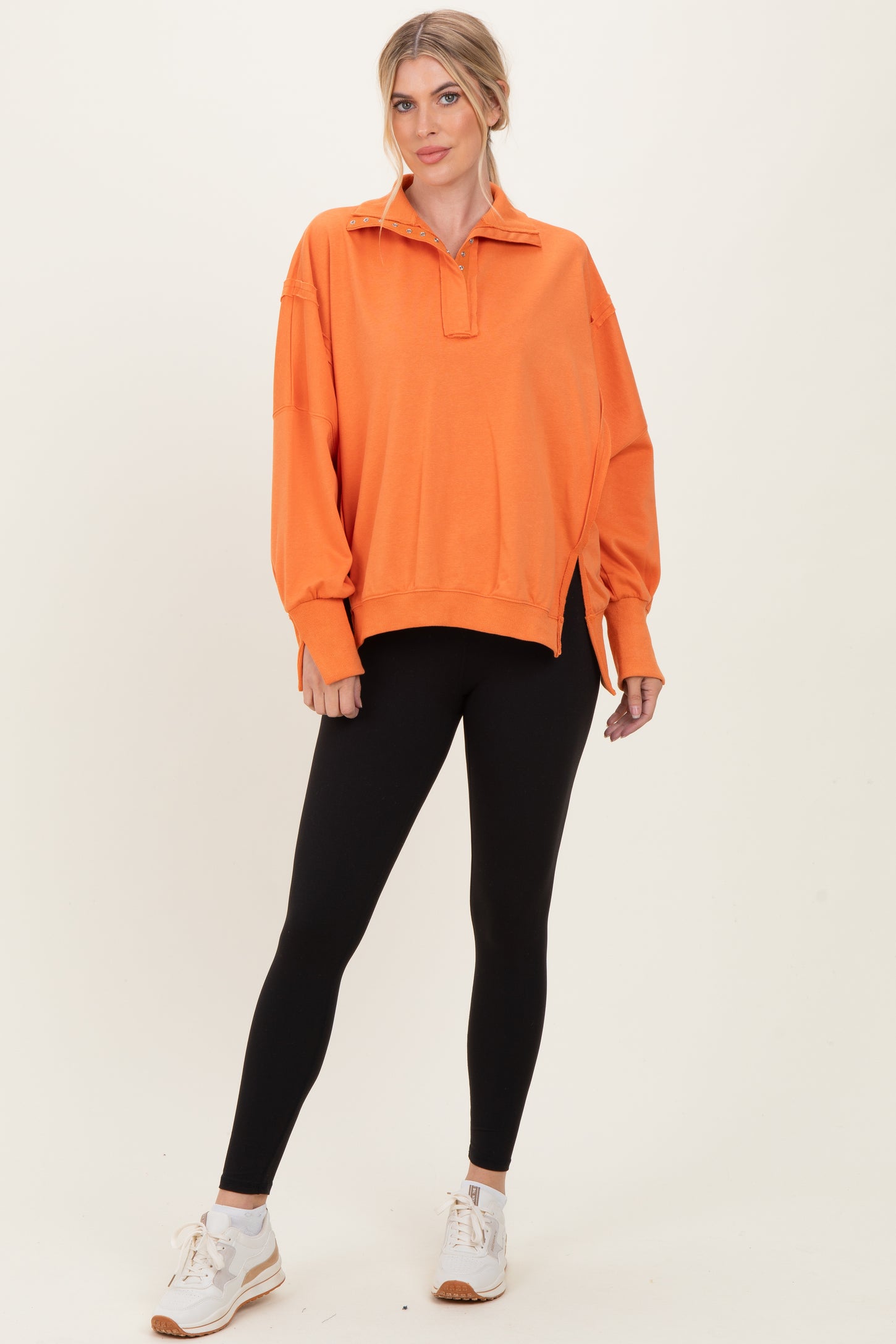 woman wearing an orange oversized pullover sweatshirt with a half zip and black leggings