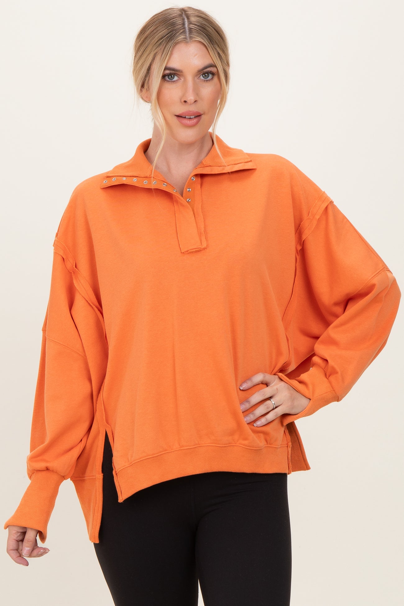woman wearing an oversized orange pullover with a quarter zip and studded collar details