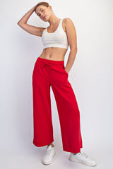woman wearing a white crop top and red wide-leg sweatpants, posing with one hand on her hip and wearing white sneakers