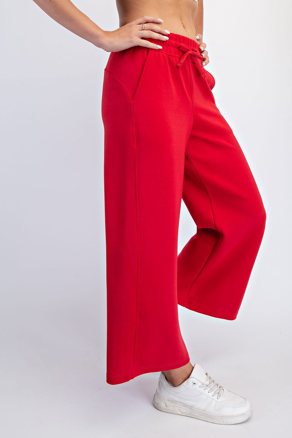 woman wearing bright red wide-leg sweatpants with pockets and a drawstring waist, styled with white sneakers