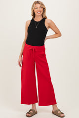 woman wearing a black sleeveless top and red wide-leg maternity pants, smiling with one hand on her hip