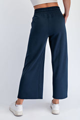woman wearing dark navy wide-leg sweatpants, viewed from the back with a white cropped top and sneakers