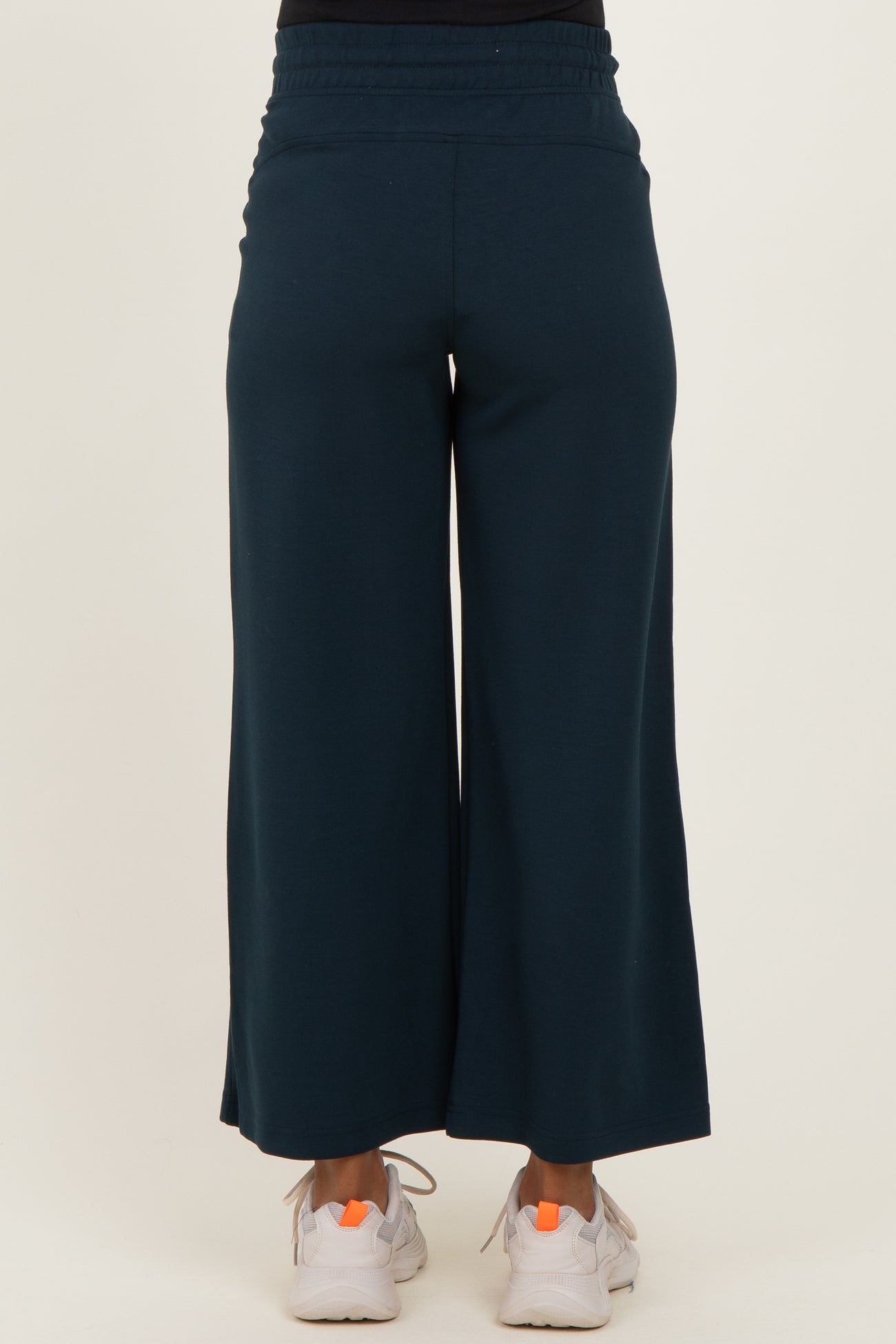 woman wearing dark teal maternity wide-leg pants, showing the back view with a comfortable waistband and casual sneakers