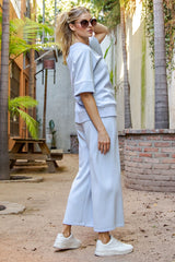 woman wearing a light blue oversized sweatshirt and matching wide-leg pants, styled with white sneakers and sunglasses