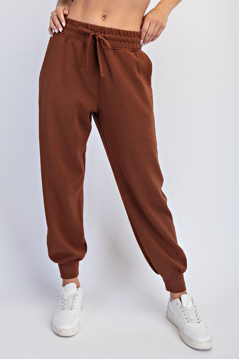 woman wearing brown sweatpants with an elastic waistband and cuffed ankles, paired with white sneakers