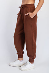 woman wearing brown high-waisted joggers with pockets and cuffed ankles, paired with white sneakers