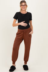 woman wearing a black short sleeve maternity top and brown jogger pants, holding her baby bump