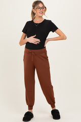 woman wearing a black short sleeve maternity top and brown maternity joggers, holding her baby bump