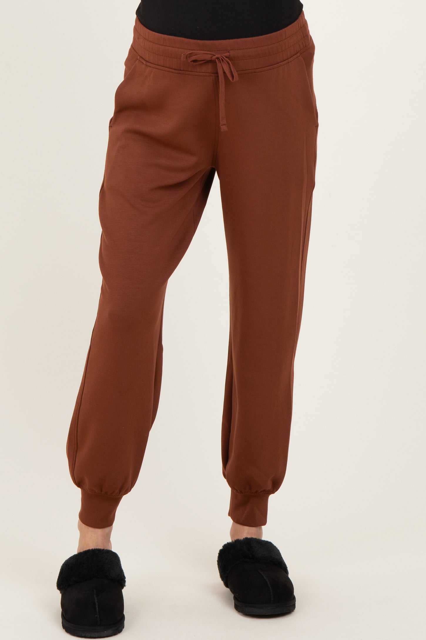 woman wearing brown maternity jogger pants with an elastic waistband and ankle cuffs, paired with black slippers