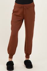 woman wearing brown maternity jogger pants with an elastic waistband and ankle cuffs, paired with black slippers