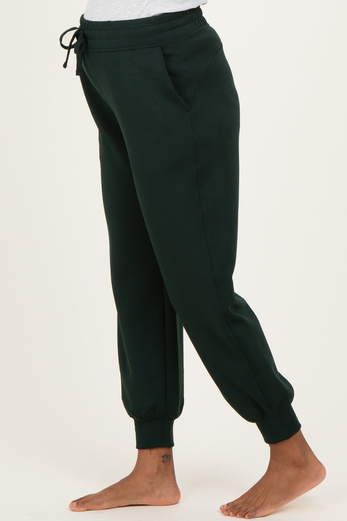woman wearing dark green maternity jogger pants with side pockets and elastic cuffs, showing a comfortable fit