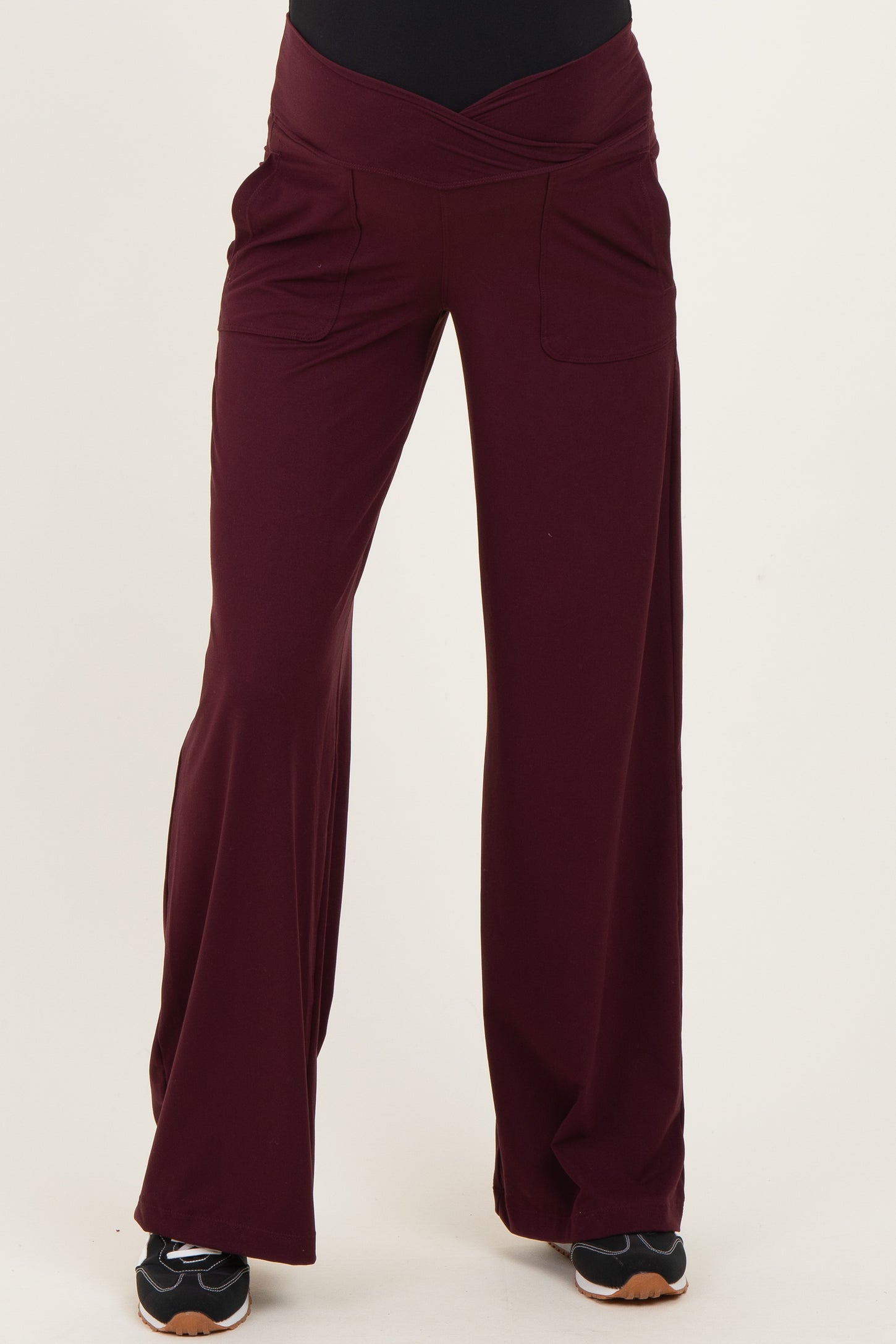 maternity wear in burgundy wide-leg pants with a crossover waistband and front pockets, model standing with hands on hips