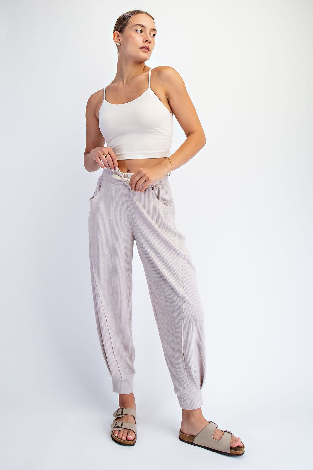 woman wearing a white cropped tank top and light pink ribbed jogger pants with pockets and slide sandals