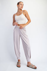 woman wearing a white cropped tank top and light pink ribbed jogger pants with pockets and slide sandals
