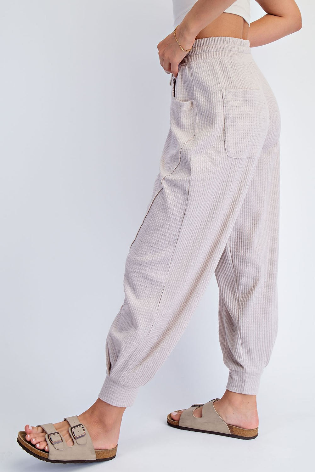 woman wearing light beige ribbed jogger pants with side pockets and adjustable waistband, styled with sandals