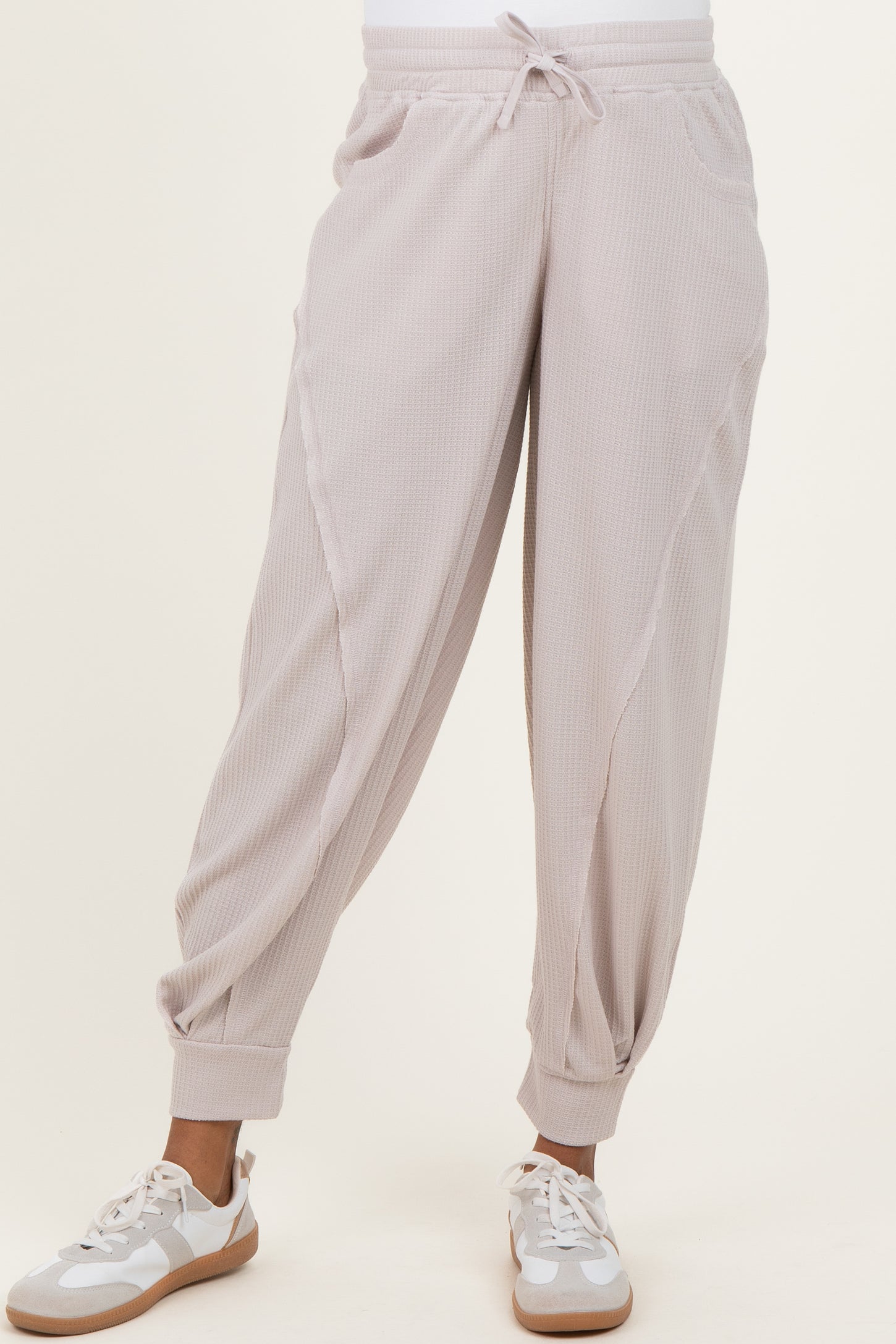 woman wearing light pink maternity joggers with side pockets and elastic cuffs, styled with white sneakers