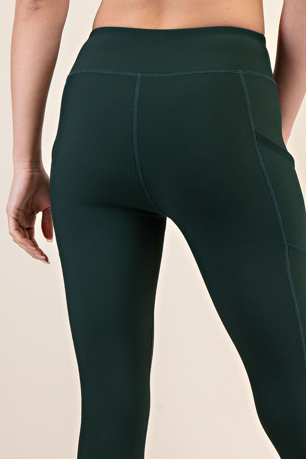woman wearing dark green ribbed high-waisted leggings, focus on back view and seam detailing