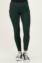 woman wearing dark green maternity leggings with a high waistband and pockets, styled with black sneakers