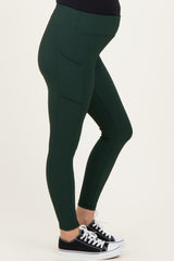 maternity wear dark green ribbed leggings with side pockets, model showing a baby bump