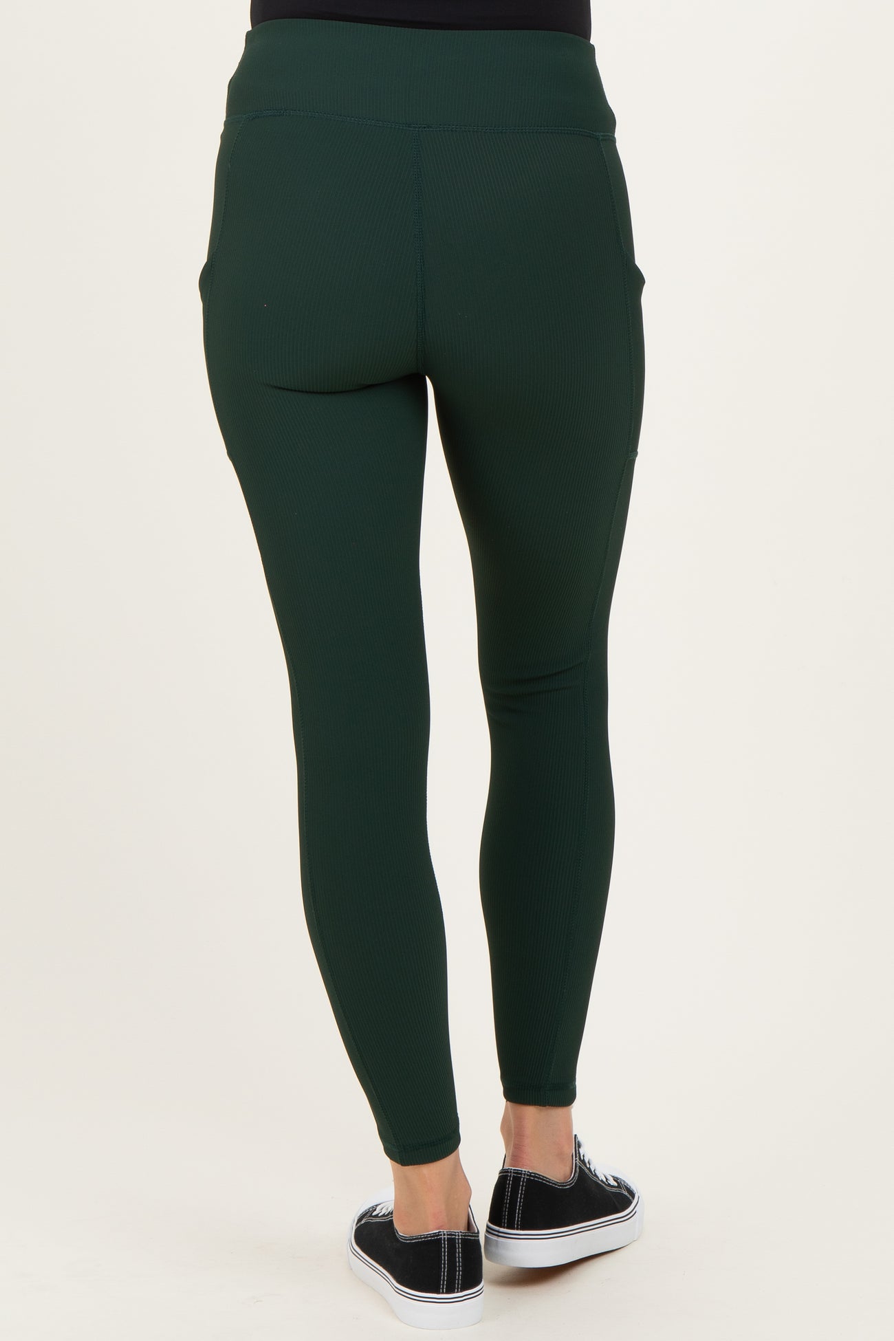 woman wearing dark green maternity leggings with a fitted style and side pockets, seen from the back
