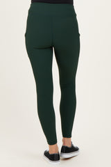 woman wearing dark green maternity leggings with a fitted style and side pockets, seen from the back