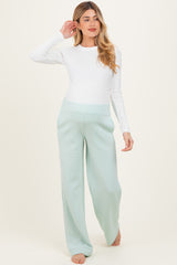 woman wearing a white long sleeve maternity top and mint green wide-leg maternity pants, baby bump visible