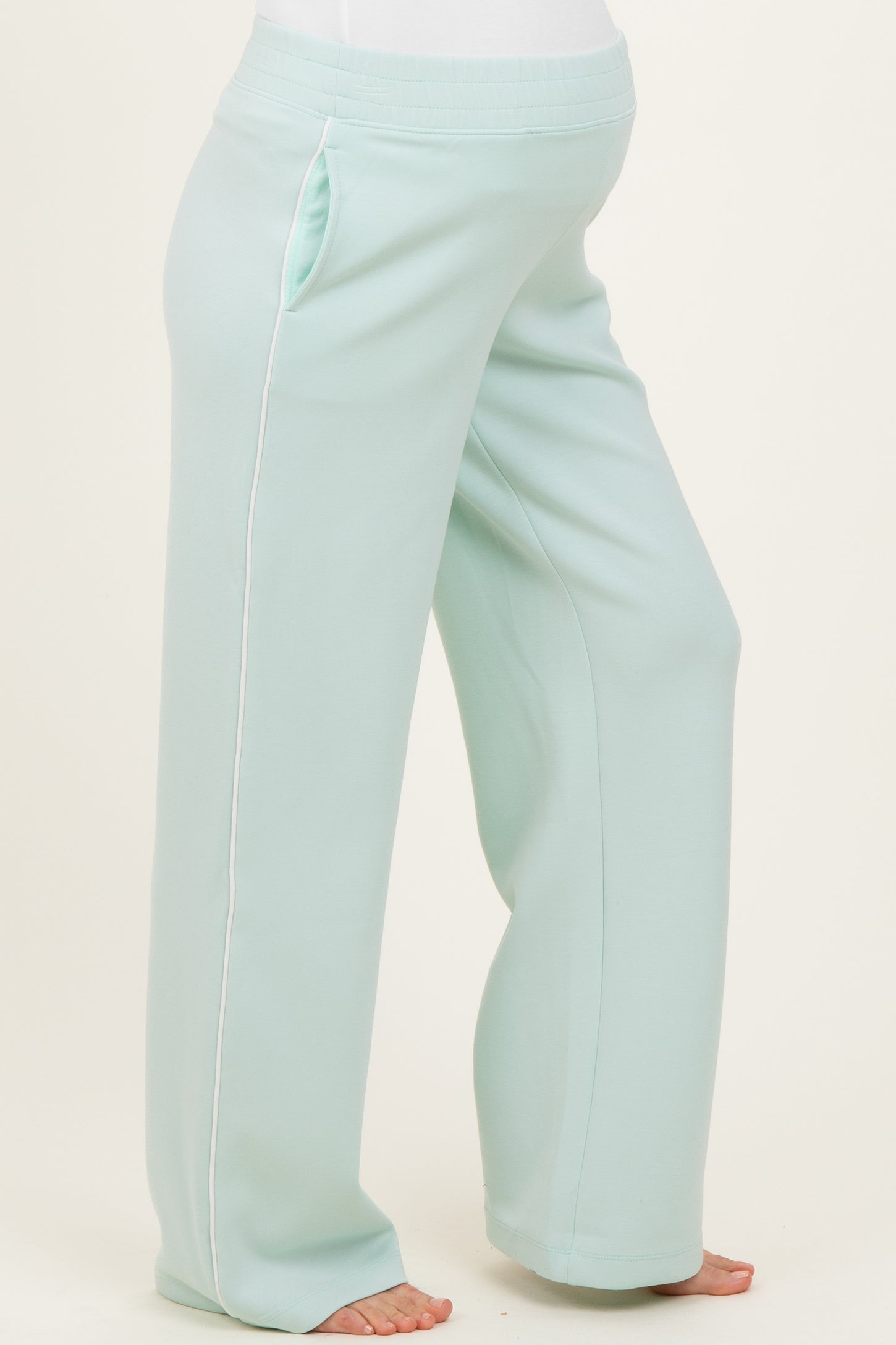 woman wearing light mint green maternity pants with side pockets and white piping, showcasing her baby bump
