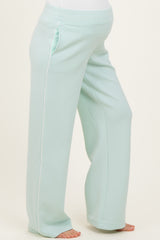 woman wearing light mint green maternity pants with side pockets and white piping, showcasing her baby bump
