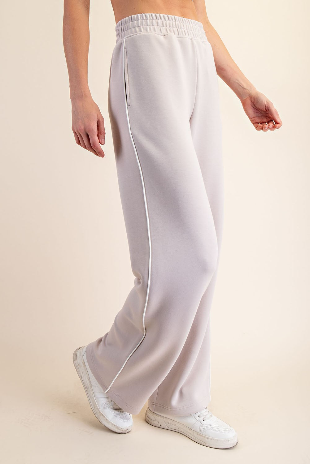 woman wearing light gray wide-leg sweatpants with side pockets and a drawstring waist, paired with white sneakers