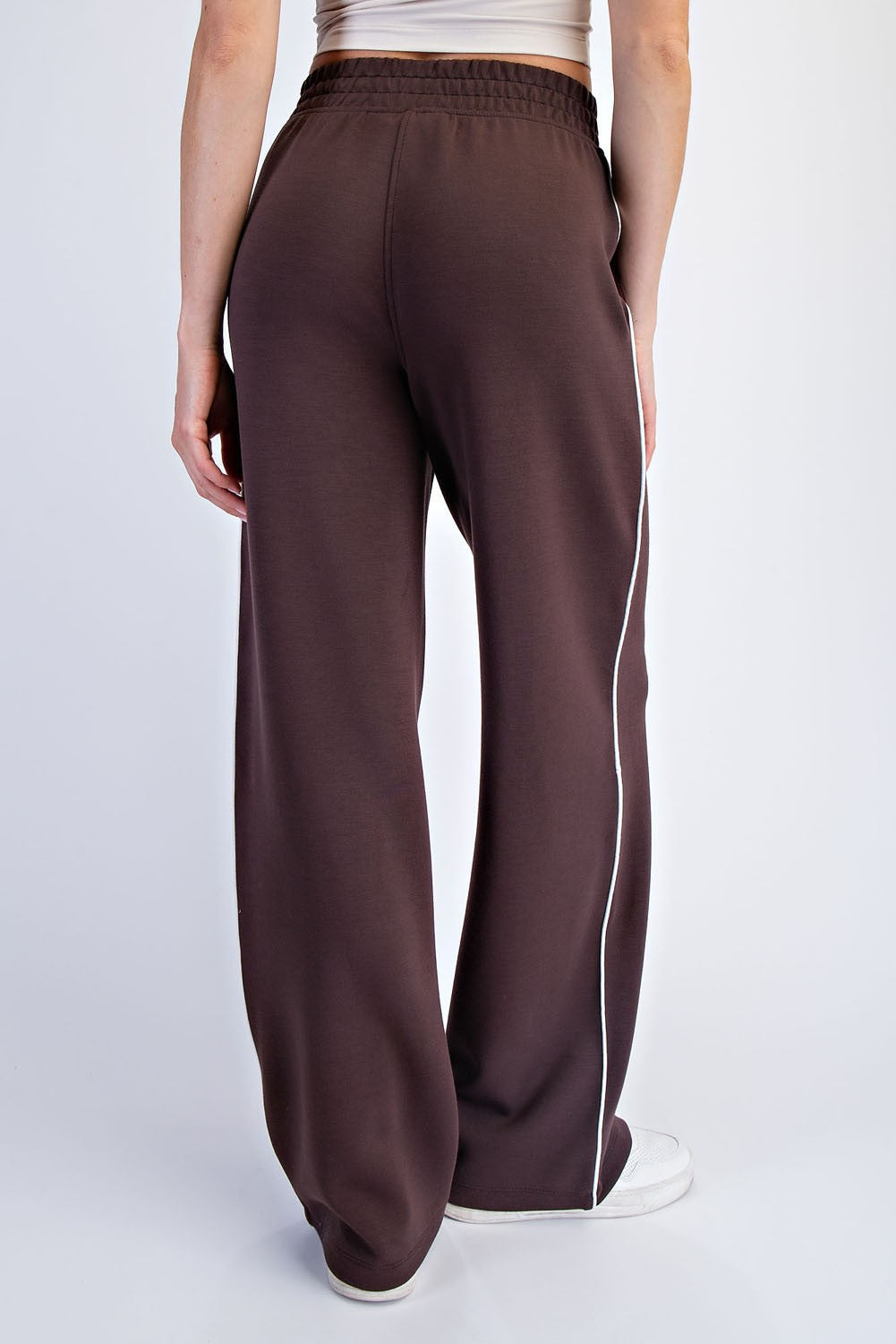 woman wearing brown wide-leg sweatpants with a white side stripe, showing the back view