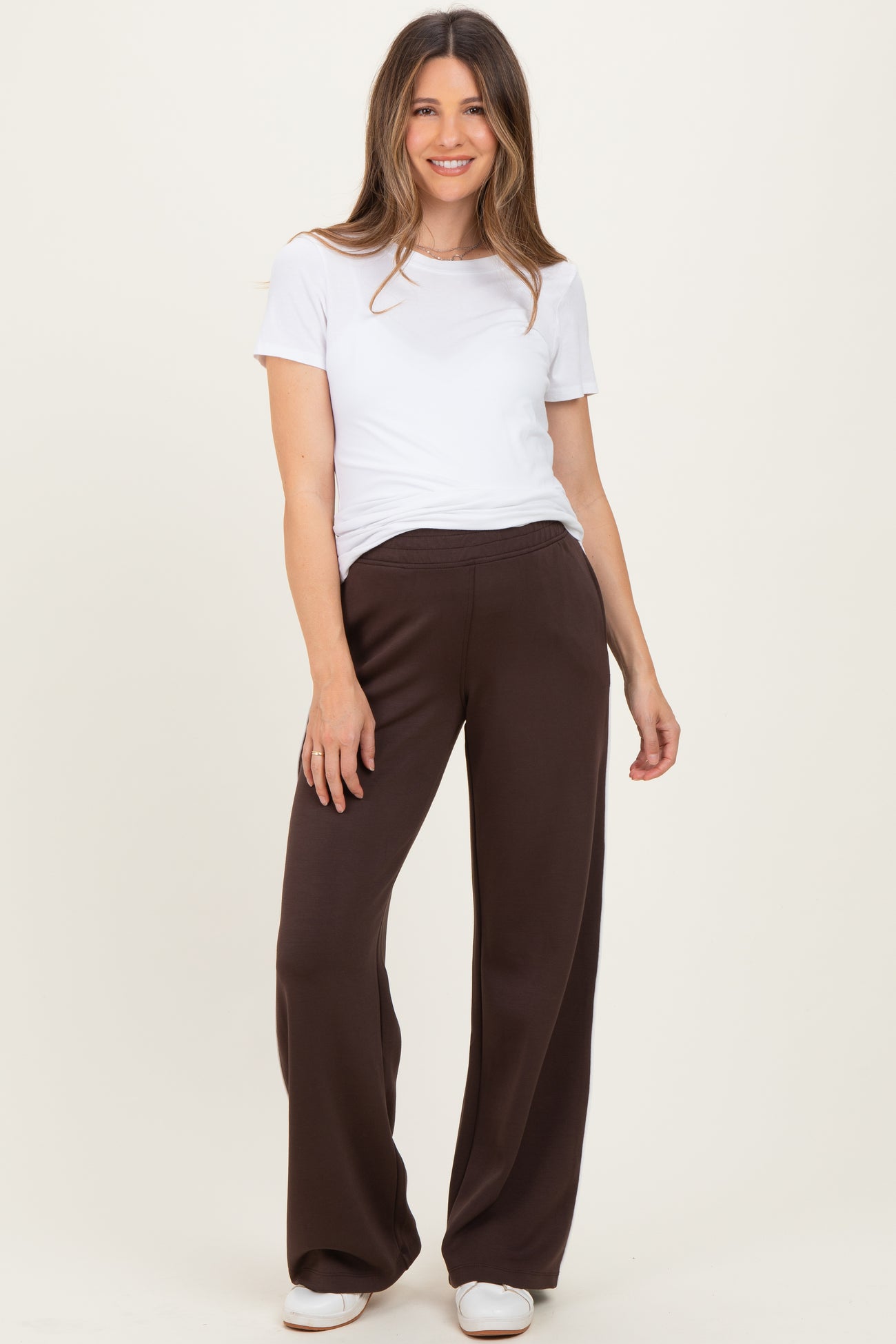 woman wearing a white short sleeve top and brown maternity wide-leg pants, posing with a relaxed smile
