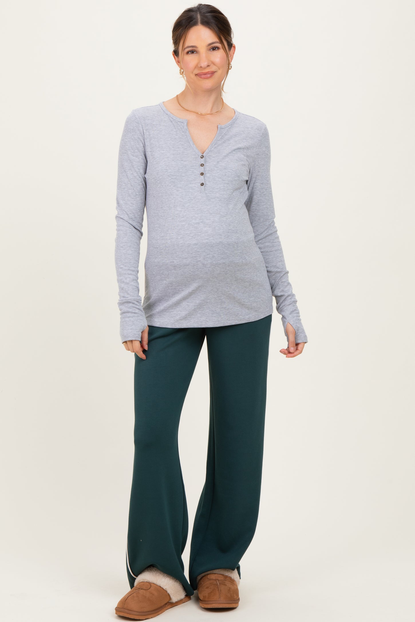 woman wearing a gray long sleeve maternity top with buttons and green maternity pants, showing her baby bump