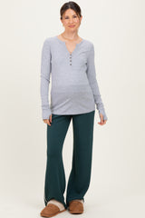 woman wearing a gray long sleeve maternity top with buttons and green maternity pants, showing her baby bump
