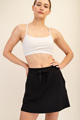 woman wearing a white cropped sports bra and a black drawstring skirt