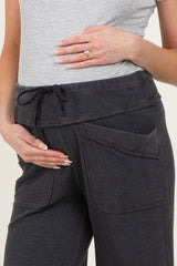 woman wearing dark gray maternity loungewear pants with a drawstring waist and side pockets, cradling her baby bump
