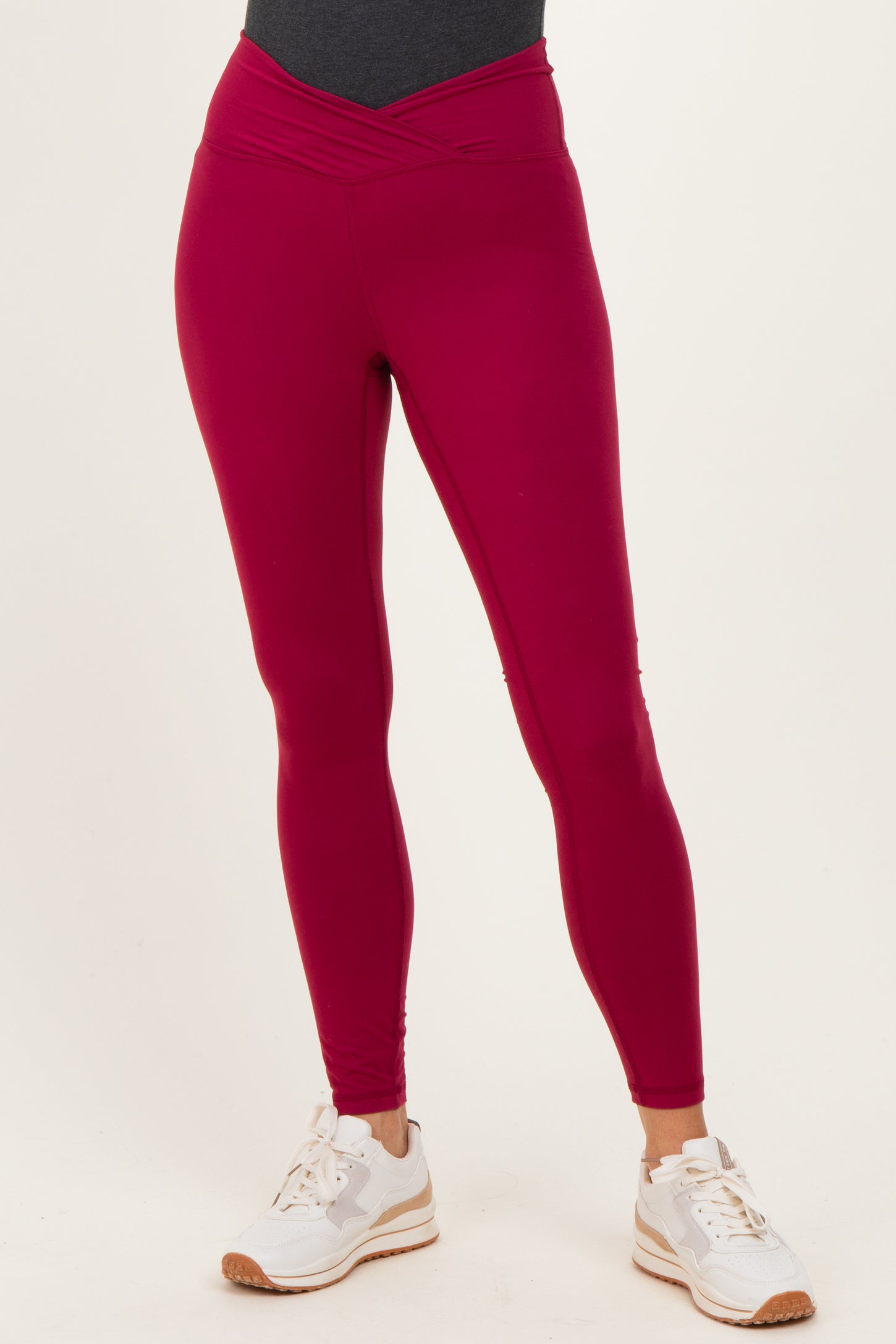 woman wearing fuchsia high-waisted active leggings with a crossover waistband and white sneakers